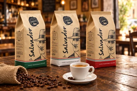 שלוש אריזות פולי קפה Salvador של 1 ק"ג, Barista, Gold ו-Mulato, ליד כוס אספרסו ופולי קפה